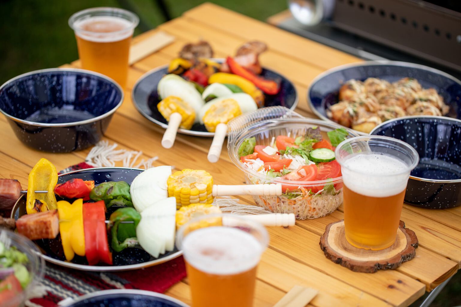 Grilled veggies and a fresh salad sit on a wood patio table with beers 